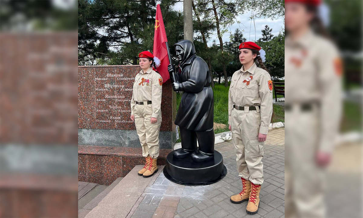 Hai cô gái đứng bên tượng người phụ nữ Ukraine cầm cờ Liên Xô được dựng tại quảng trường thành phố Mariupol ngày 5/5. Ảnh: RIA Novosti.