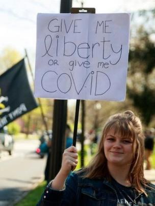 A protester holds a placard: "Give me liberty or give me Covid"